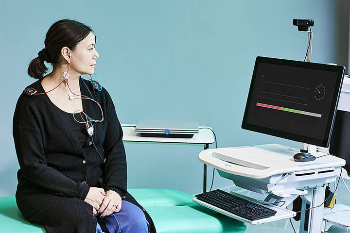 Patient sat on examination bed with cVEMP electrode montage and looking toward a computer screen with an EMG monitor. The Interacoustics Eclipse is resting on a table next to the patient.