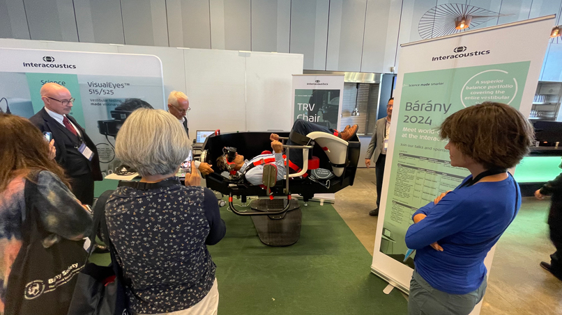 A group of attendees and Interacoustics staff at Bárány 2024 observing an attendee strapped into the TRV Chair in a horizontal position