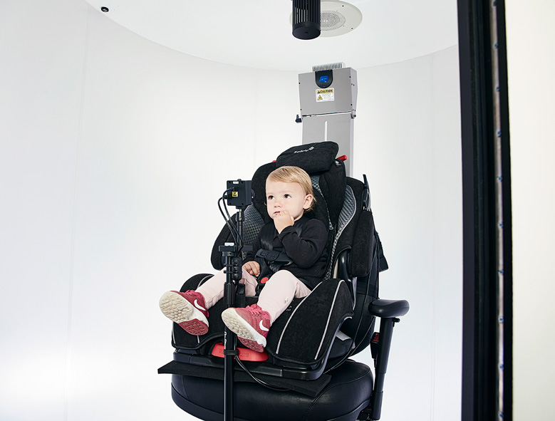 Little girl sitting in car seat, looking toward an in-booth camera.