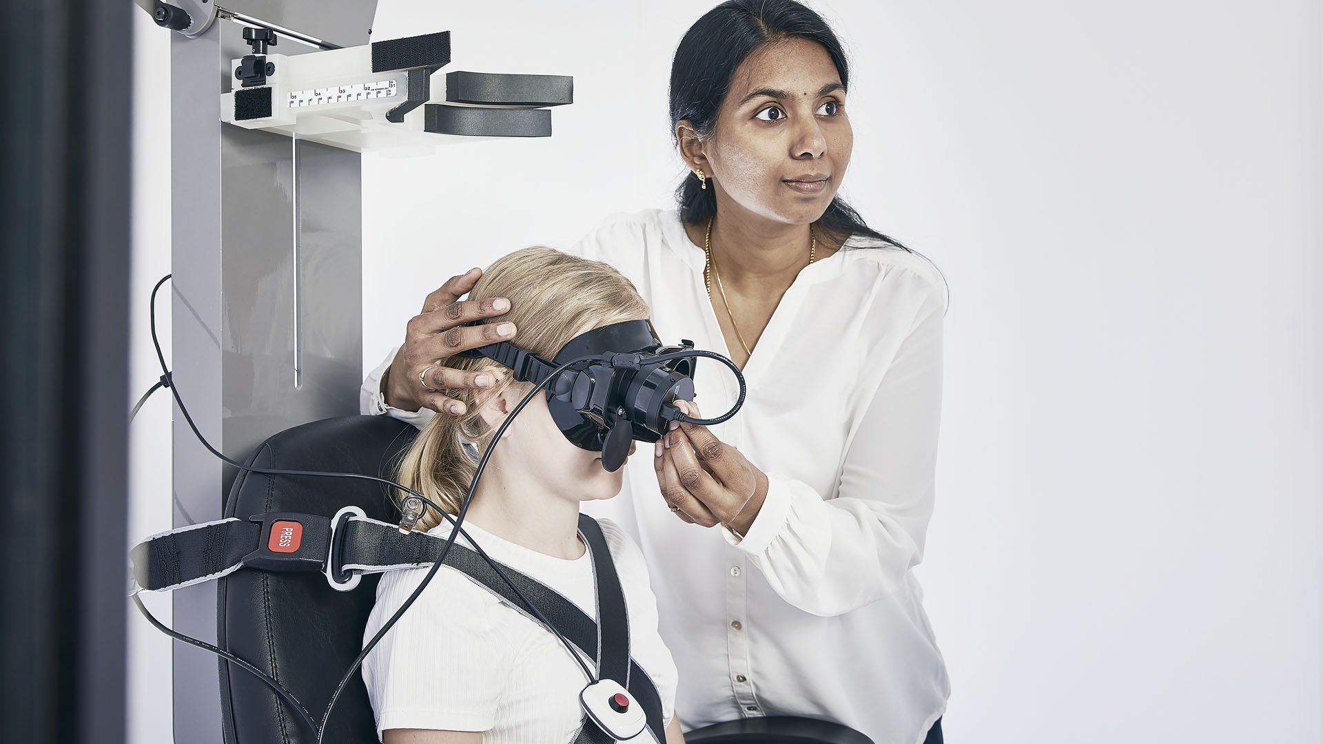 Female clinician adjusting small face VNG goggle on young female patient, who is fixated in Orion Comprehensive chair