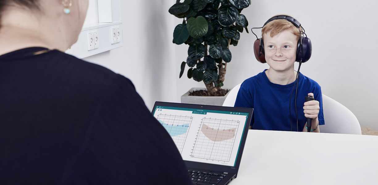 Boy holding patient response button, facing toward female clinician. Luna software displayed on laptop.