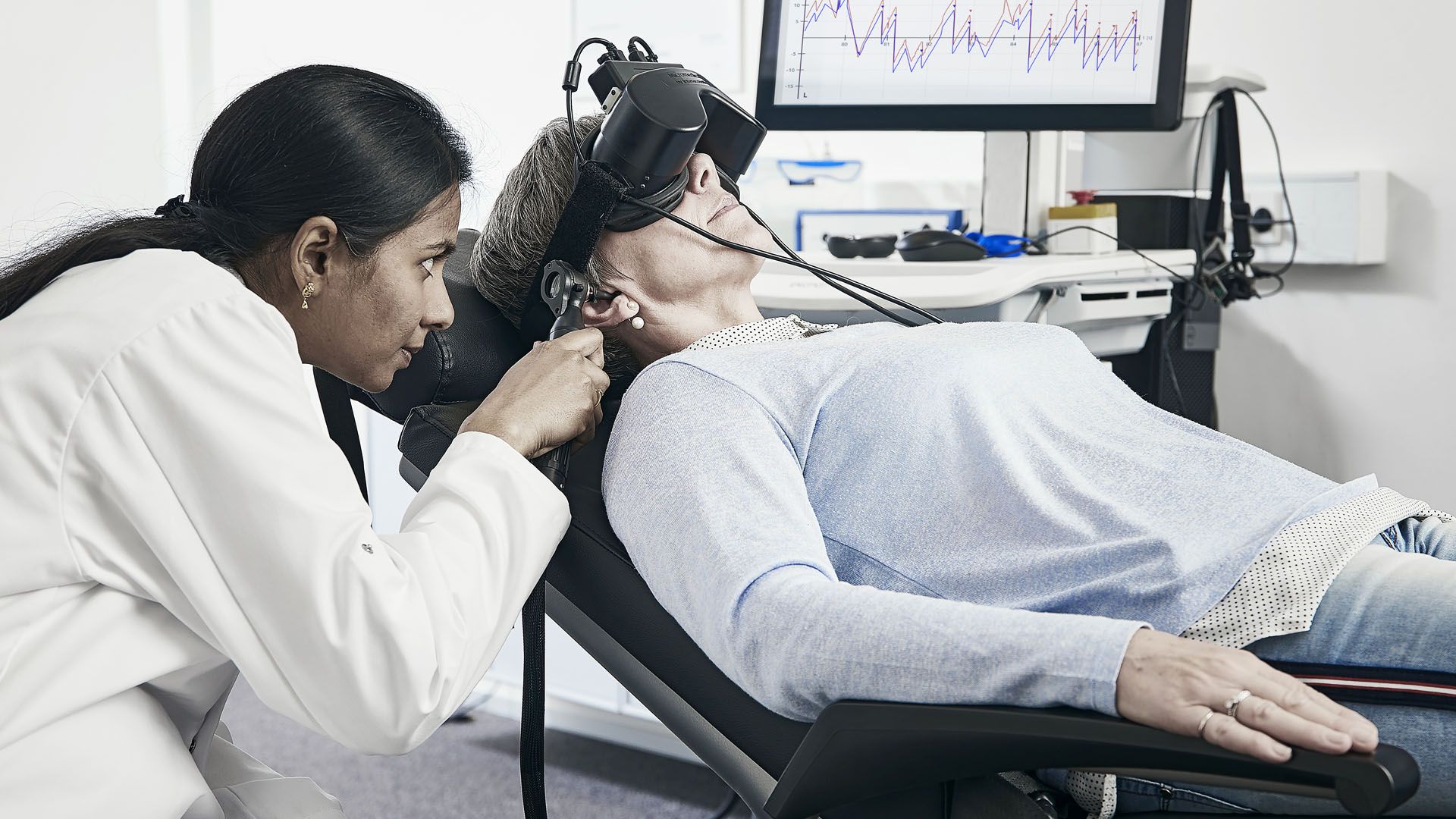 Female clinician performing caloric irrigation on female patient fixated with VNG goggles in Orion Reclining chair in a supine position