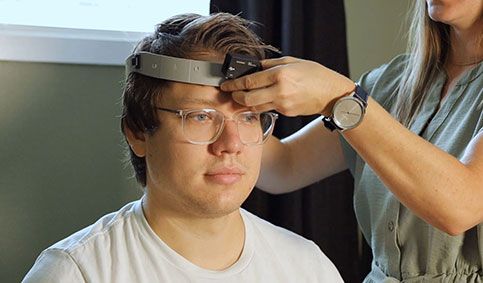 Clinician attaching VORTEQ™ head sensor to a headband fixated on a young man's head