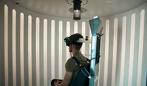 Patient strapped into the enclosed Orion Comprehensive chair and wearing VNG goggles. The light from the optokinetic drum above the patient is displaying a visual pattern across the wall of the booth enclosure.