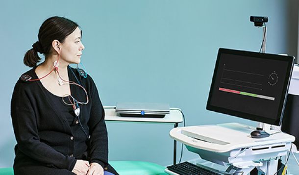 Patient sat on examination bed with cVEMP electrode montage and looking toward a computer screen with an EMG monitor. The Interacoustics Eclipse is resting on a table next to the patient.