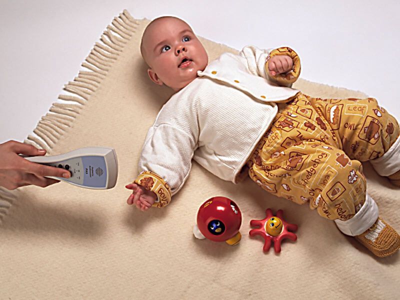 Young baby boy lying on a carpet with toys. Clincian holding the PA5 audiometer close to his right ear