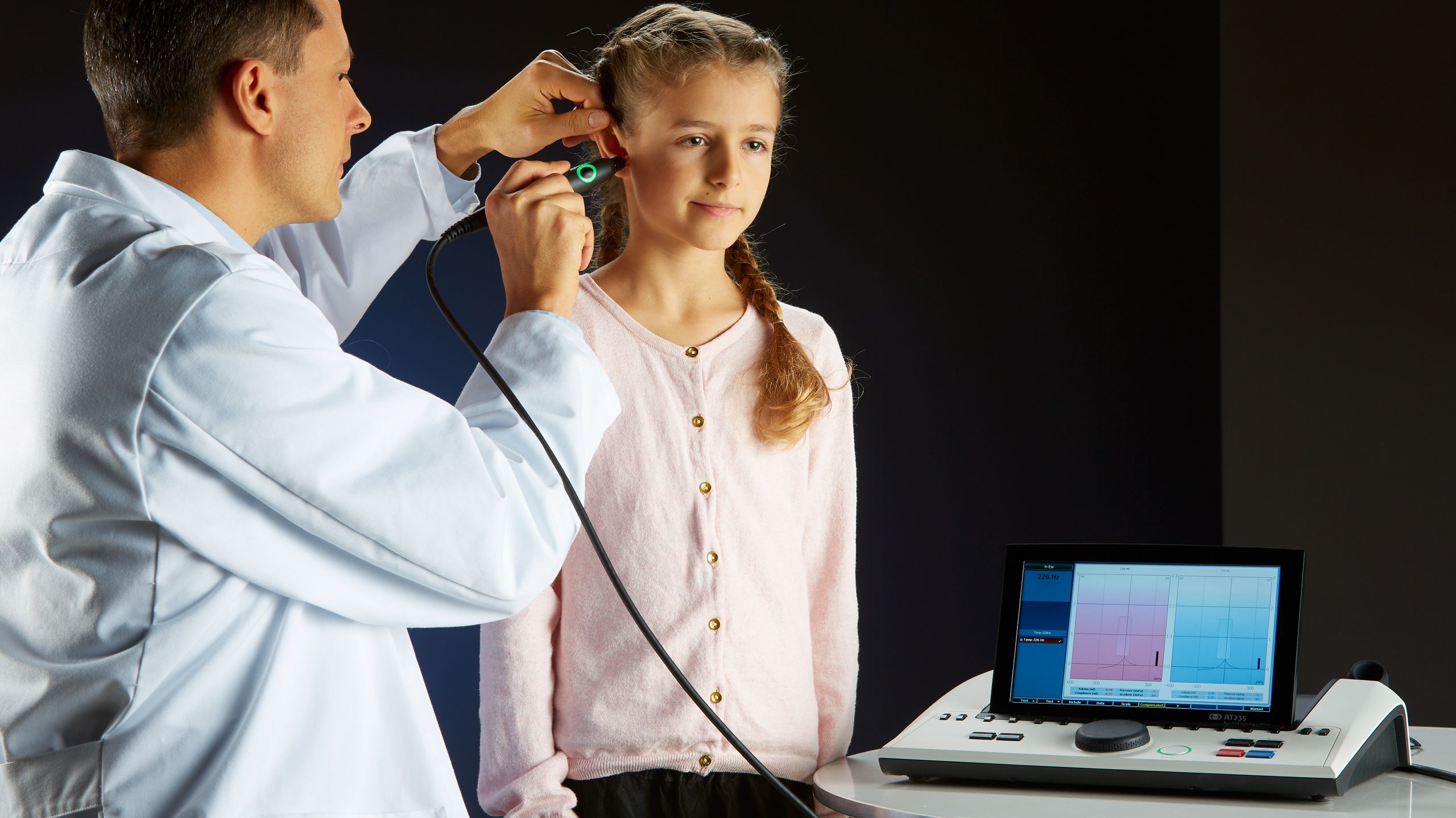 Male clinician using diagnostic probe to perform middle ear assessment on young female patient
