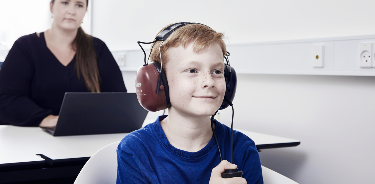 Boy holding patient response button, facing away from female clinician.