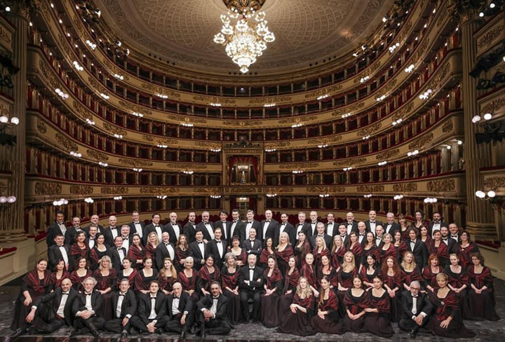 The large groups of choir singers and musicians from the orchestra posing for a photo in the beautiful Teatro alla Scala, with a stunning chandelier hanging from its ceiling.