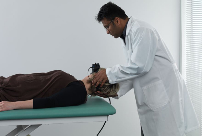 Male clinician performing head roll to the right on female patient. The patient is lying in a supine position and wearing VNG goggles.
