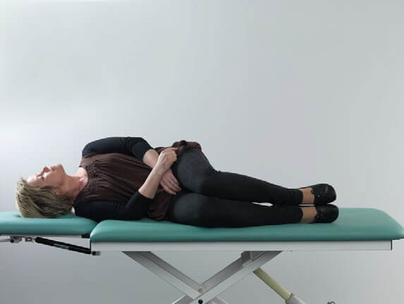 Female patient in black clothes lying on her right side on examination table. She has her head turned about 90 degrees toward the left.