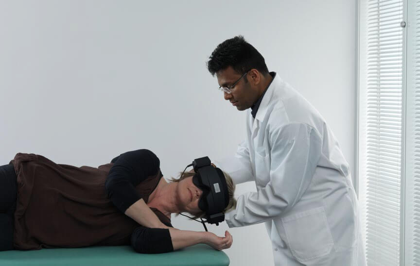 Male clinician rolling female patient onto her left. The patient is visibly wearing VNG goggles.