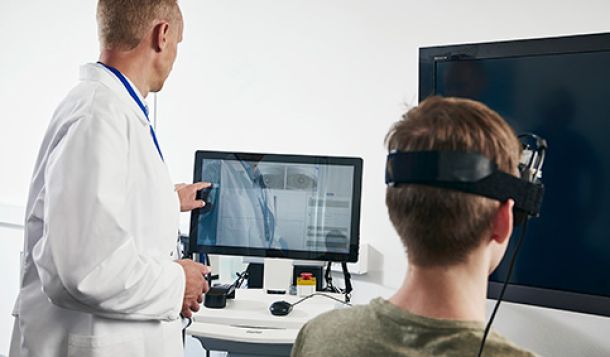 Clinician operating VisualEyes software on touch screen while patient wearing VNG goggles is looking toward a flat screen TV