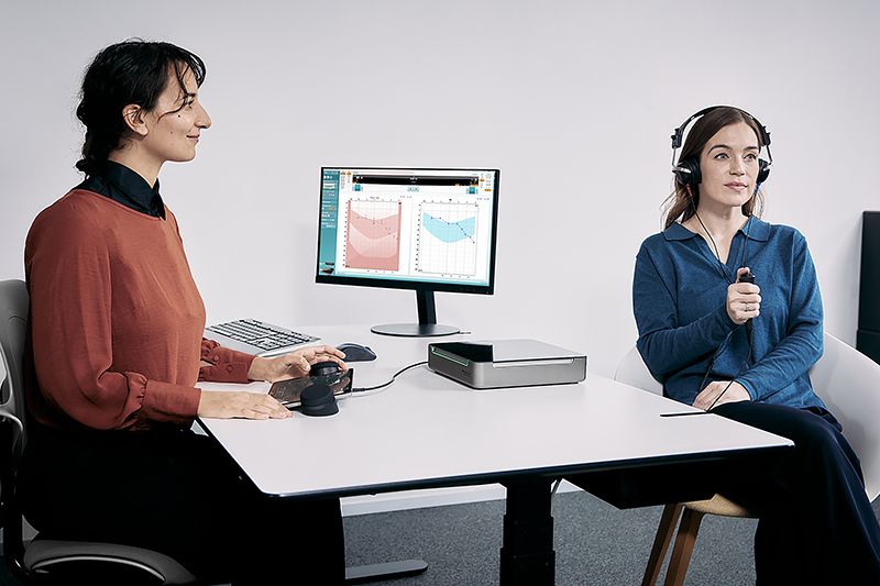 A clinician using the Equinox Evo and Touch Keyboard to perform audiometry in an adult patient sat across the desk from the clinician
