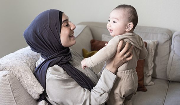 Parent and child enjoying a precious moment on their sofa. The parent is holding the child and the child is smiling and wearing a hearing aid.