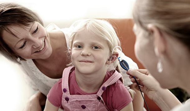 Female clinician performing real-ear measurement in young girl that is sat on her mother's lap