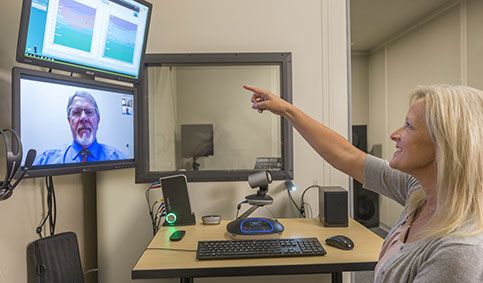 Female patient pointing toward audiometry software with male clinician looking on remotely via web cam
