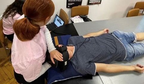 Two audiology students performing supine positional test in patient wearing VNG goggles