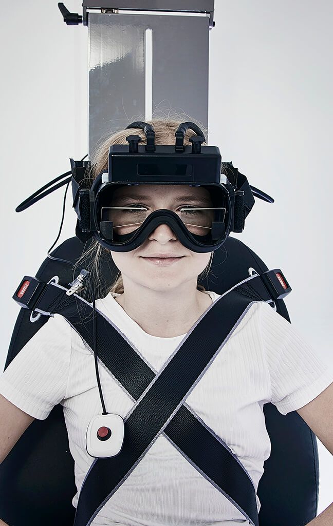 Frontal view of girl strapped into Orion Auto Traverse rotary chair, wearing VisualEyes VNG goggles