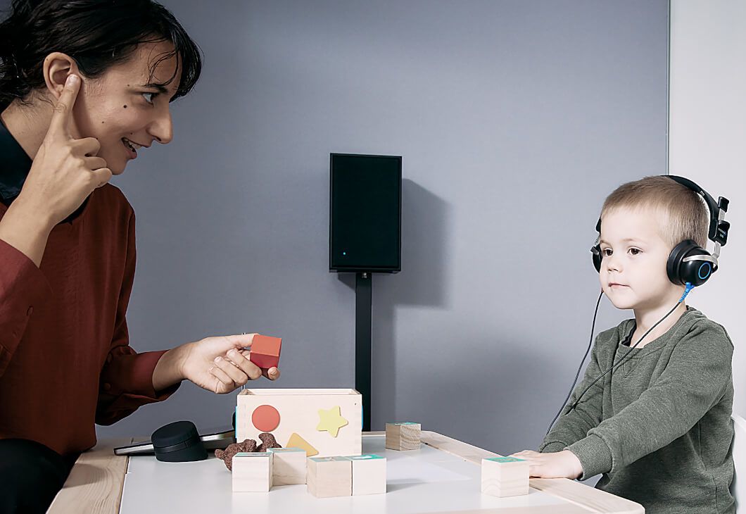With the use of play audiometry, an audiologist is performing a hearing test on a child who is wearing headsets. 