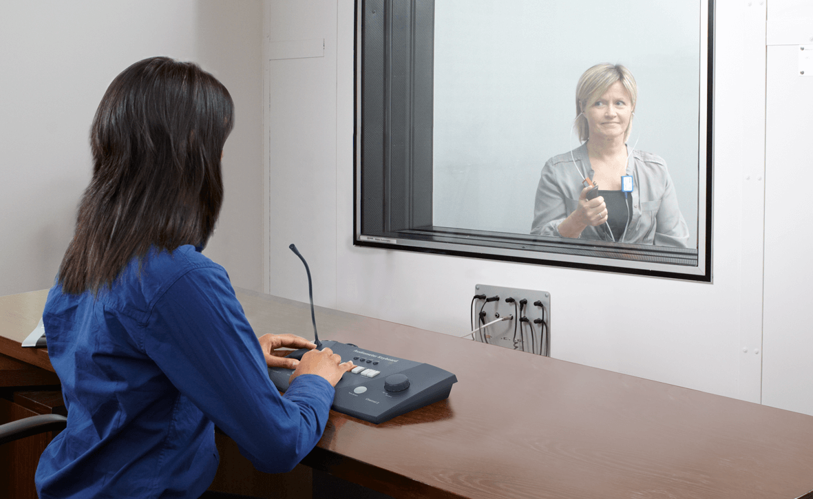 Female clinician performing audiometry with a female patient in booth pressing response switch button