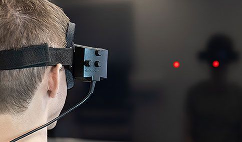 Man wearing VNG goggles and looking toward TV screen with two red dots
