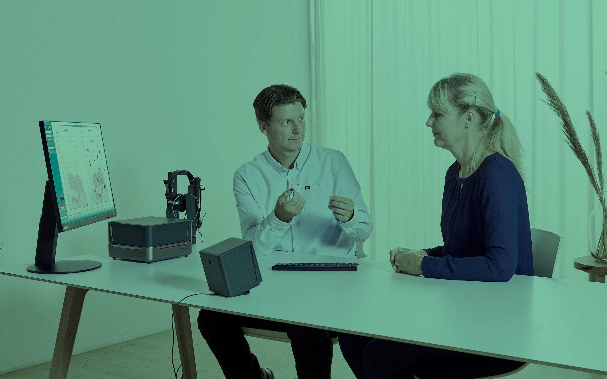 Male clinician showing a hearing aid to his female patient.