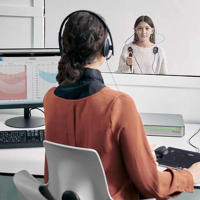 Un facultativo usando el Equinox Evo y el Touch Keyboard para realizar una audiometría en un adolescente sentado en una cabina.