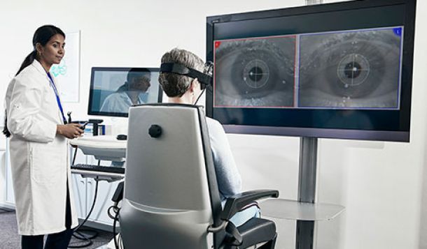 Female clinician performing VNG test on female patient. TV screen showing eye imagery with torsional tracking.