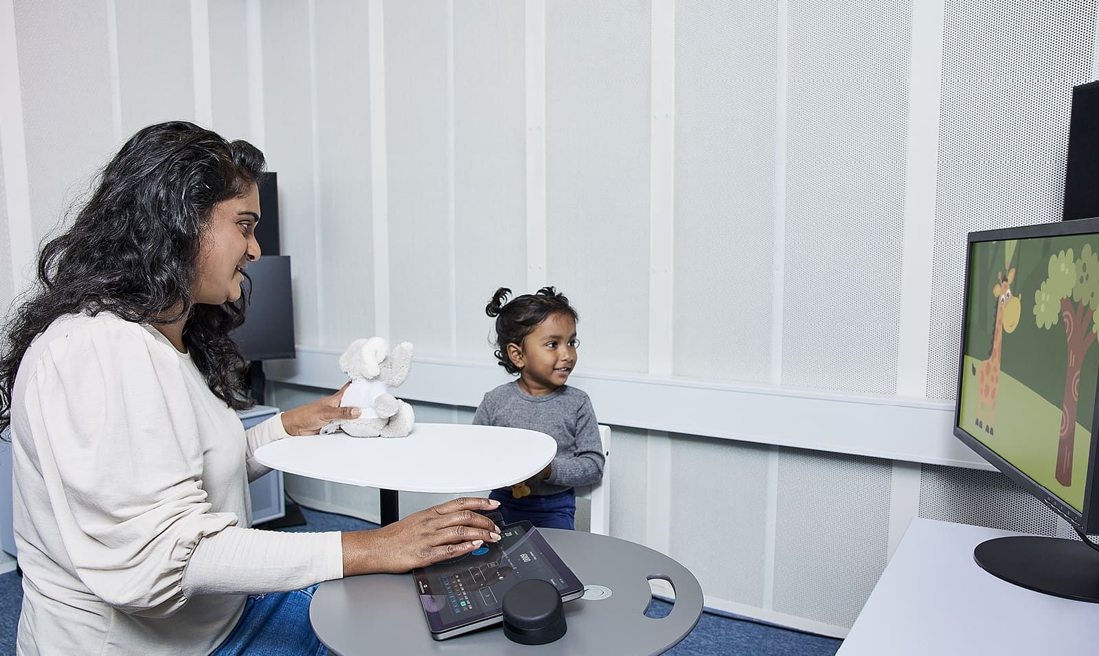 A clinician sitting in booth with a young child and using the Touch Keyboard to perform visual reinforcement audiometry
