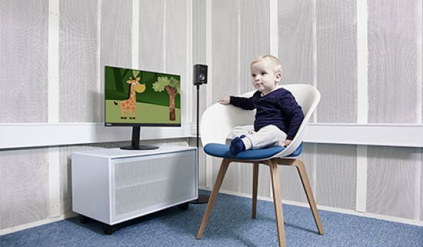 Little boy sat in a white chair next to a computer screen showing an animated giraffe